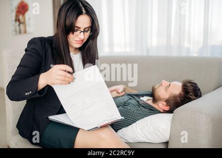 Betonte Mann liegt auf Sofa bei psychotherapeut Rezeption. Ärztin schreibt Notizen in Notepad, professionelle Psychologie Unterstützung Stockfoto