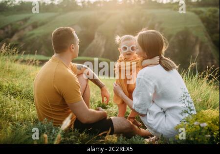 Familie mit kleiner Tochter ruht beim Wandern auf der Wiese auf Schluchten Hintergrund. Rückansicht. Stockfoto