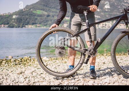 Fahrradreparatur. Mann Repariert Mountainbike. Radfahrer Mann in Schwierigkeiten Hinterrad Fall eines Unfalls. Mann repariert Fahrrad in der Nähe von See in Stockfoto