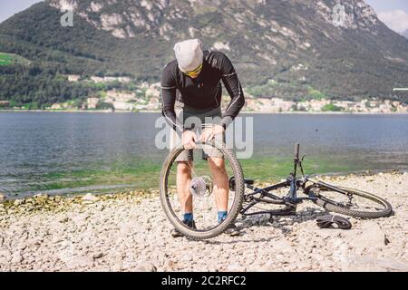 Fahrradreparatur. Mann Repariert Mountainbike. Radfahrer Mann in Schwierigkeiten Hinterrad Fall eines Unfalls. Mann repariert Fahrrad in der Nähe von See in Stockfoto