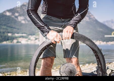 Fahrradreparatur. Mann Repariert Mountainbike. Radfahrer Mann in Schwierigkeiten Hinterrad Fall eines Unfalls. Mann repariert Fahrrad in der Nähe von See in Stockfoto