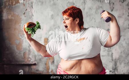 Übergewichtige Frau mit hantel und Sandwich in den Händen, Kampf gegen Fettleibigkeit, Übergewicht problem. Junk Food essen Stockfoto