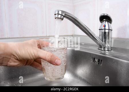 Hand hält Glas Wasser aus Küchenarmatur gegossen Stockfoto