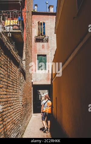 Tourist mit einem orangen Rucksack und Bandana Spaziergänge entlang der engen Straße in Europa. Italien Venedig im Sommer. Die Fassade des alten Hauses Stockfoto