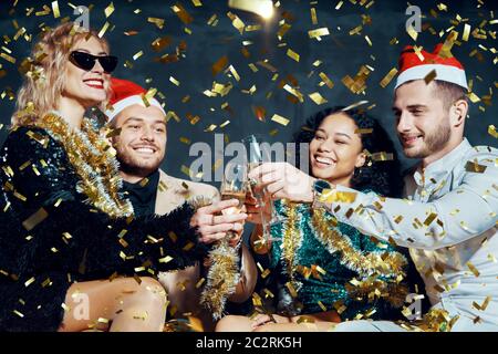 Multiethnische glückliche Freunde toasten mit Champagner zu Weihnachten oder Neujahr, gratulieren einander und genießen Teil Stockfoto