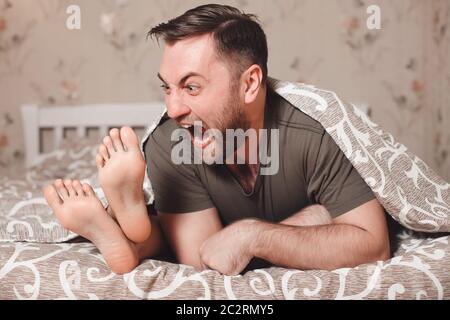 Verspielter Mann versucht, Frau die Füße im Bett beißen. Stockfoto