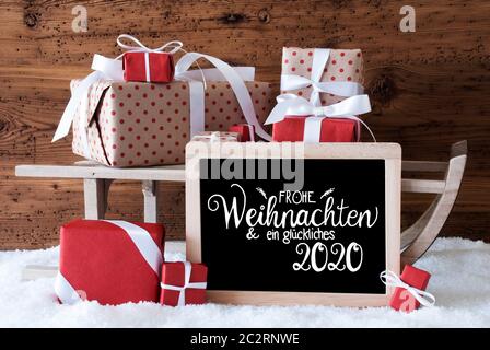 Tafel mit Deutschen Kalligraphie Frohe Weihnachten und ein Glueckliches 2020 bedeutet, frohe Weihnachten und einen guten Rutsch ins Jahr 2020. Schlitten mit Weihnachtsgeschenk und Pr Stockfoto