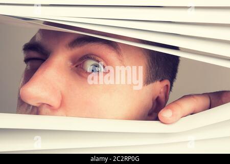 Ein junger Mann, Blick durch Fenster-Vorhänge Stockfoto