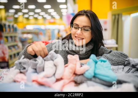 Fröhliche Zukunft Mutter in Gläser kauft Baby Kleidung im Store für Neugeborene. Schwangere Frau im Shop von Waren für Kleinkinder Stockfoto