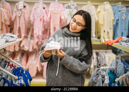 Lächelnd zukünftige Mutter wählt Baby Hut in der Store für Neugeborene. Schwangere Frau im Shop von Waren für Kleinkinder Stockfoto