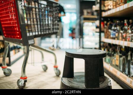 Warenkorb zwischen Regalen mit alkoholischen Getränken, niemand. Reihen von Flaschen im Supermarkt, verwischen Hintergrund Stockfoto
