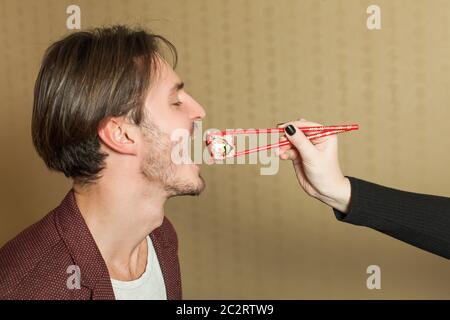 Weibliche Hand füttert den Mann mit Essstäbchen. Japanische Küche Stockfoto