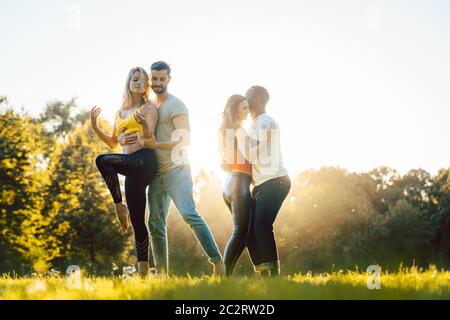 Zwei Paare machen während des Sonnenuntergangs in einem Park fortgeschrittene Tanzbewegungen Stockfoto