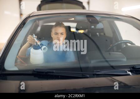 Frau reinigt die Windschutzscheibe des Autos mit Spray, Blick von