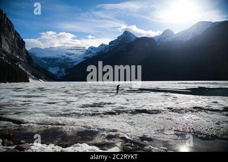 Ein einsamer Mann geht an einem sonnigen Tag auf der gefrorenen Oberfläche des Lake Louise, Banff National Park, Alberta, Kanada Stockfoto