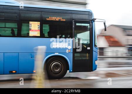 Blauer Bus fährt schnell auf der Regenstraße auf der Straße an launisch bewölktem bewölktem Tag Stockfoto