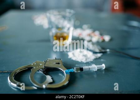 Junky Kit, Betäubungsmittel Konzept, sucht Problem. Die Pillen sind auf Holztisch, Spritze für Dosis, Alkohol und Handschelle, Draufsicht ausgelegt Stockfoto