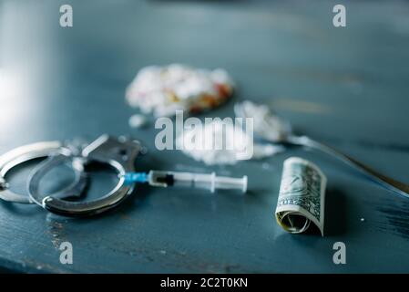 Junky Kit, Betäubungsmittel Konzept, sucht Problem. Die Pillen sind auf Holztisch, Spritze für Dosis, Alkohol und Handschelle, Draufsicht ausgelegt Stockfoto
