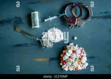 Junky Kit, Betäubungsmittel Konzept, sucht Problem. Die Pillen sind auf Holztisch, Spritze für Dosis, Alkohol und Handschelle, Draufsicht ausgelegt Stockfoto