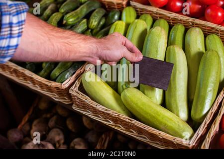 Verkäufer Hand stellt den Preis Tag auf roten Tomaten in Holzkorb gelagert. Stockfoto