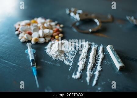 Junky Kit, Betäubungsmittel Konzept, sucht Problem. Die Pillen sind auf Holztisch, Spritze für Dosis, Alkohol und Handschelle, Draufsicht ausgelegt Stockfoto