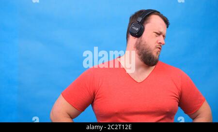 Bärtig lustig niedlich fetten Mann in einem rosa T-Shirt hört Musik und tanzt auf einem blauen Hintergrund, close-up, Copy Space. Stockfoto
