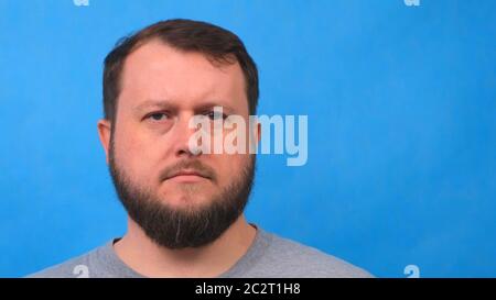 Porträt eines traurigen bärtigen Mannes in einem grauen T-Shirt, der auf blauem Hintergrund singt und mit der Kamera spricht. Stockfoto