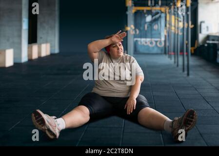 Müde übergewichtige Frau sitzt auf dem Boden in der Turnhalle. Kalorien verbrennen, adipösen weiblichen Person in Sport Club, fette Leute Stockfoto