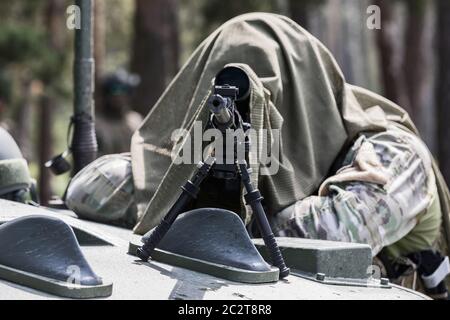 Militärmann in Tarnuniform mit Gewehr. Ausgerüstet Scharfschützenschießen mit Gewehr. Ein maskierter Scharfschütze zielt auf ein Ziel. Scharfschütze mit einem Gewehr. Stockfoto