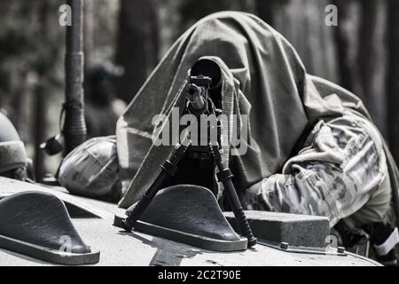 Militärmann in Tarnuniform mit Gewehr. Ausgerüstet Scharfschützenschießen mit Gewehr. Ein maskierter Scharfschütze zielt auf ein Ziel. Scharfschütze mit einem Gewehr. Stockfoto