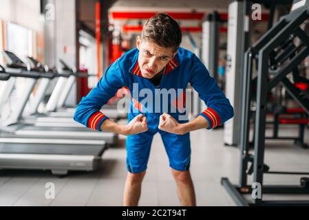 Dünne Mann in Sportswear zeigt seine Muskeln an der Turnhalle, Humor. Männliche Person im Sport Club schwach Stockfoto