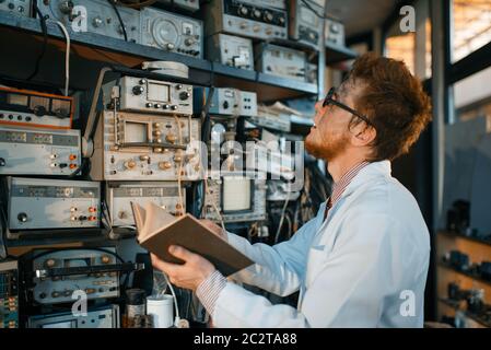 Seltsamer Ingenieur mit Buch, Test im Labor. Elektrische Messgeräte im Hintergrund Laborausrüstung, Ingenieurwerkstatt Stockfoto