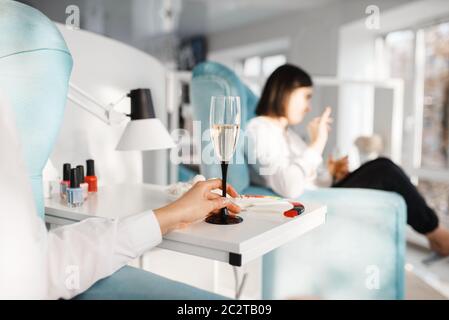 Zwei Frauen mit Champagner im Schönheitssalon. Professionelle Kosmetikerin, weibliche Kunden, Zehennagel und Fingernagel Pflege im Spa Stockfoto