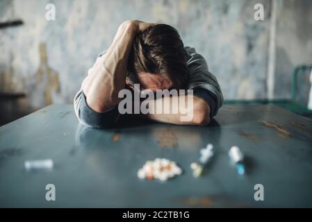 Männliche Junkie am Tisch mit Drogen und Spritze, grunge Inneneinrichtung im Hintergrund sitzen. Drogensucht Konzept, Leute süchtig Stockfoto