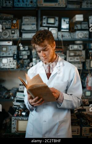 Seltsamer männlicher Wissenschaftler, der im Labor ein Buch liest. Elektrische Messgeräte im Hintergrund Laborausrüstung, Ingenieurwerkstatt Stockfoto