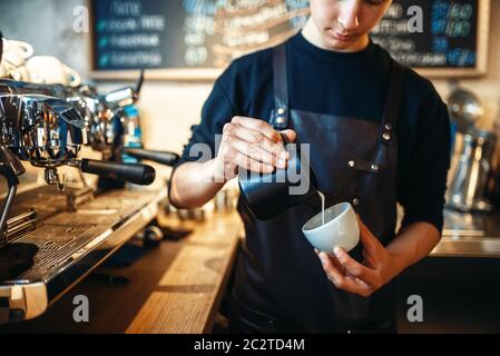 Barista in Schürze gießt Sahne in die Tasse Kaffee, cafe Zähler für den Hintergrund. Professionelle cappuccino Zubereitung durch den Barkeeper Stockfoto