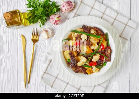 Nahaufnahme des Sommers Rinderstreifen Eintopf mit neuen Kartoffeln, Spargel und Blumenkohl in einer weißen Schüssel auf einem Holztisch, amerikanische Küche, Blick auf die Landschaft, Stockfoto