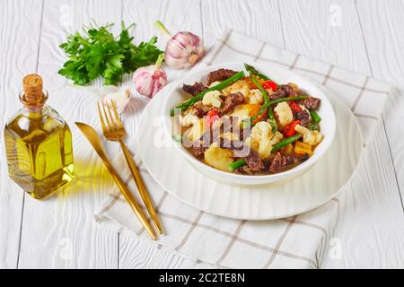 Sommer Rinderstreifen Eintopf mit neuen Kartoffeln, Spargel und Blumenkohl in einer weißen Schüssel auf einem Holztisch, amerikanische Küche, Blick auf die Landschaft Stockfoto