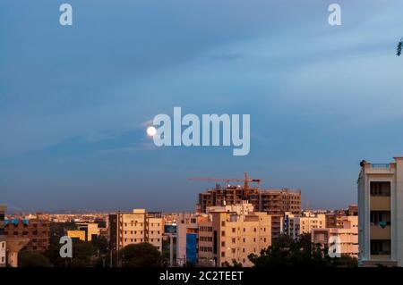 Eine dünne Wolkenschicht bedeckt den Vollmond und gibt ihm einen Heiligeneffekt, wenn er über der Stadt Hyderabad, Telangana, Indien, aufsteigt. Stockfoto