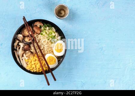 Ramen. Soba Nudeln mit gekochten Eiern, Shiitake-Pilze und Gemüse, Top-Shot auf blauem Hintergrund mit Essstäbchen, eine Tasse o Stockfoto