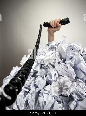 Hand mit Telefon reicht von grosser Haufen zerknülltes Papier Stockfoto