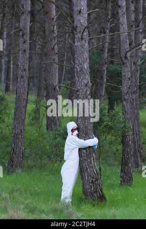 Person mit Schutzanzug umarmt zu einem Baum in einem Waldgebiet. Stockfoto