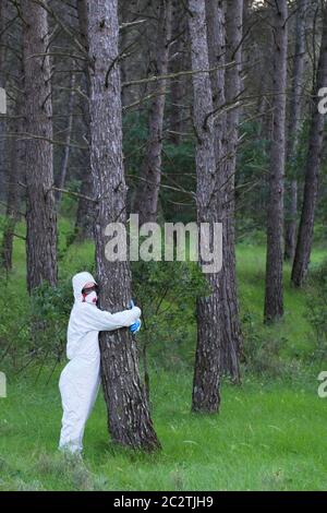 Person mit Schutzanzug umarmt zu einem Baum in einem Waldgebiet. Stockfoto