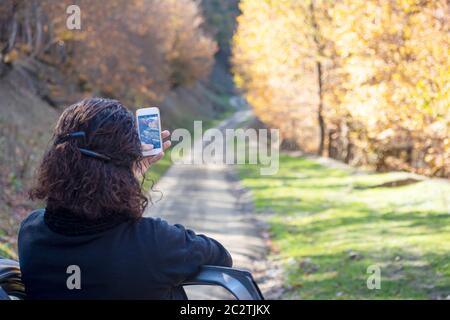 Rückseite Blick auf eine junge Frau mit Smartphone während der Herbstsaison im ländlichen Raum Stockfoto