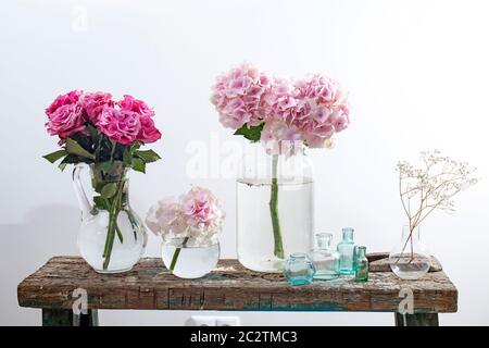 Ein Strauß roter Rosen in einer Glasvase und alt trägt einen Vintage-Koffer auf blauem Grund und zwei Birnen und auf einer hölzernen Ruinenfläche der Bank Stockfoto