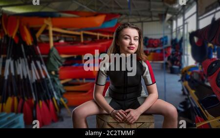 Weibliche sportman im Neoprenanzug, Boote und Ausrüstung für den Hintergrund. Bootfahren Vermietung oder Rescue station Stockfoto