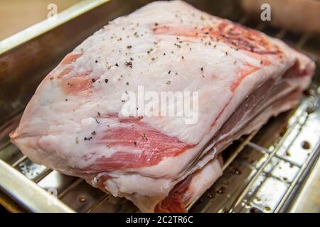 Nahaufnahme eines kleinen Lammbröckens auf einem Gestell mit Salz und schwarzem Pfeffer, fertig zum Braten im Ofen Stockfoto