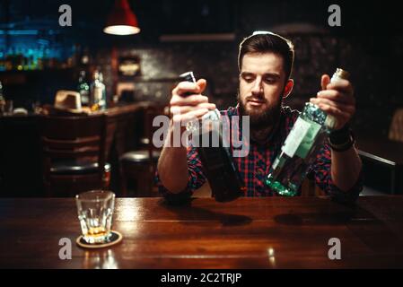 Alkoholische Sitzen an der Theke mit zwei Flaschen Alkohol trinken in Händen. Männliche Person im Pub, Alkoholismus, Trunkenheit Stockfoto
