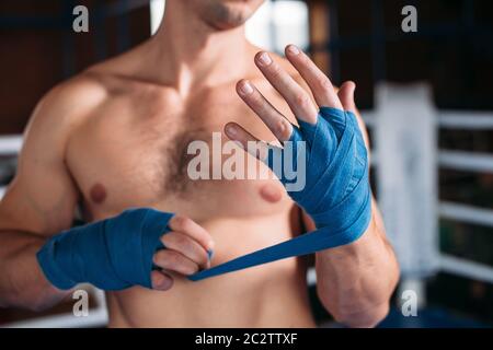 Nahaufnahme der Hand des Kraft Boxers, der Verband vor dem Kampf oder Training zieht. Boxring auf dem Hintergrund. Stockfoto