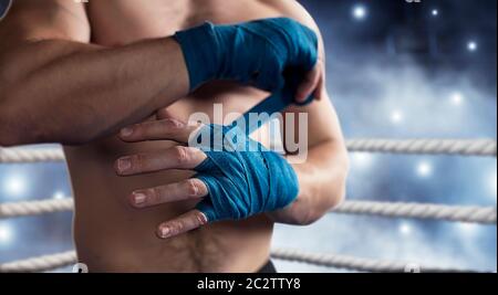 Nahaufnahme der Hand des Kraft Boxers, der Verband vor dem Kampf oder Training zieht. Boxring auf dem Hintergrund. Stockfoto